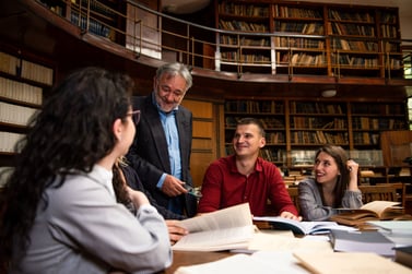A law student study group meeting in the library ask their professor a question.